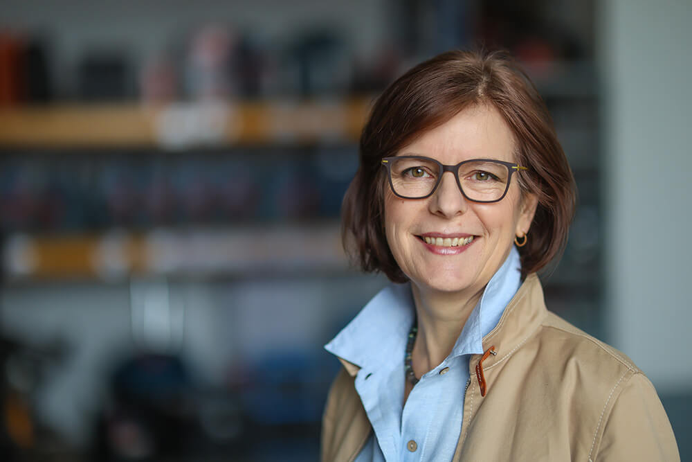 Dorothée Schartz | © Rupert Oberhäuser Eine Frau mit blauer Bluse, beigefarbener Jacke und Brille schaut lächelnd in die Kamera.