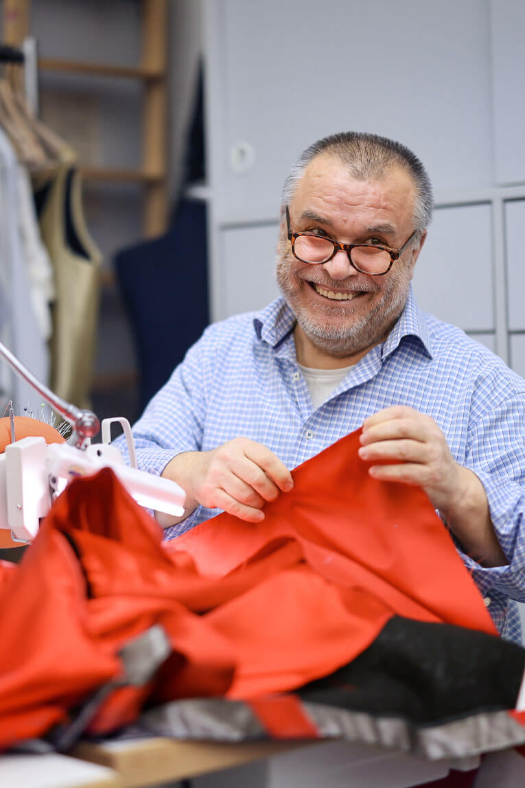 Der Herrenschneider Yusuf Aydoğan hält ein Stück Stoff in seinen Händen und lächelt in die Kamera.