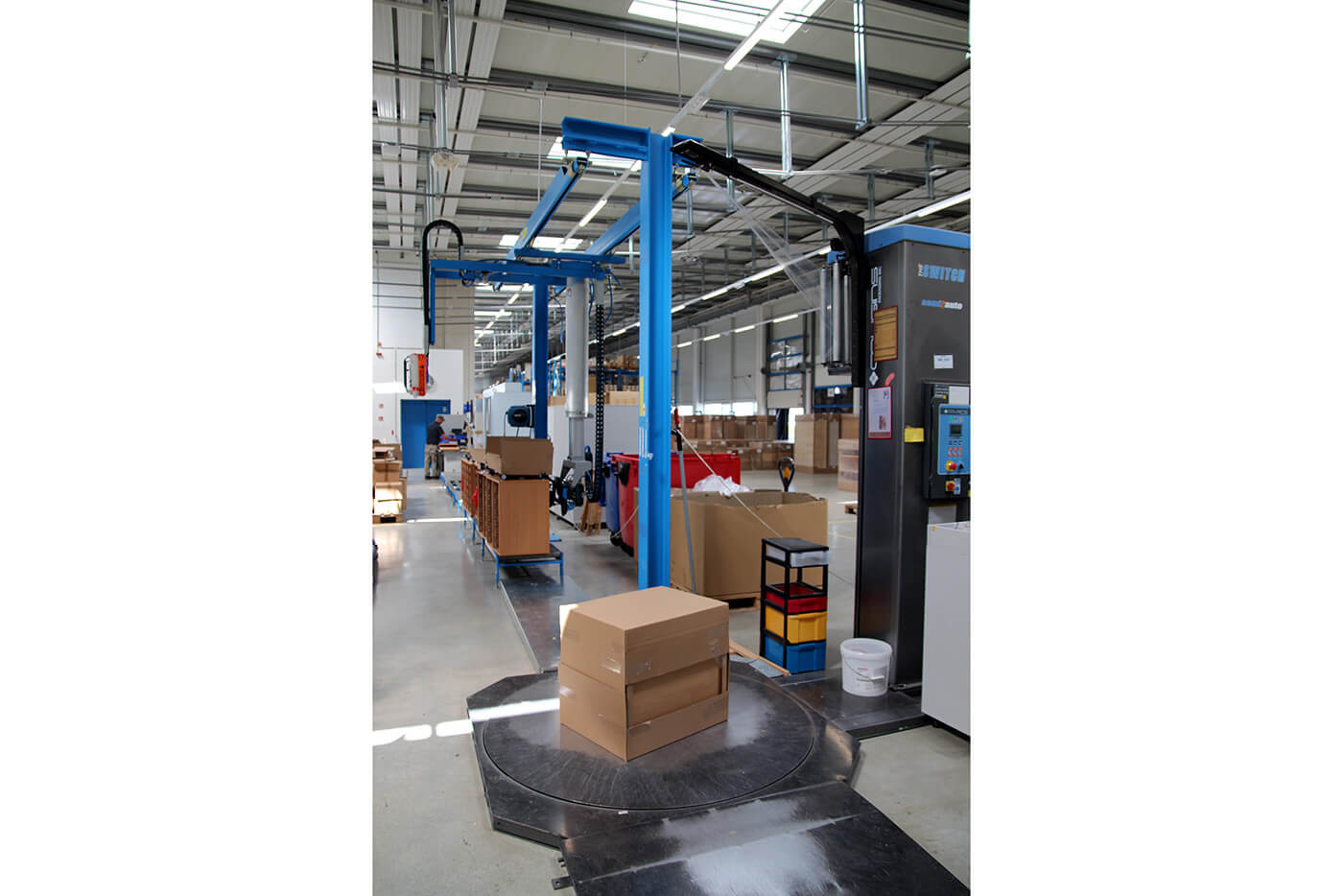 In der Arbeitshalle werden in Kartons verpackte Kleinmöbel automatisch mit Folie umwickelt.