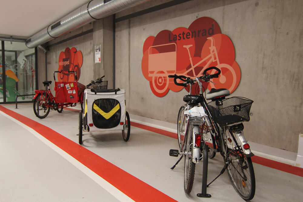 Fahrräder in der Fahrradtiefgarage. Die Abstellflächen sind mit dicken roten Streifen auf dem hellen Boden markiert.