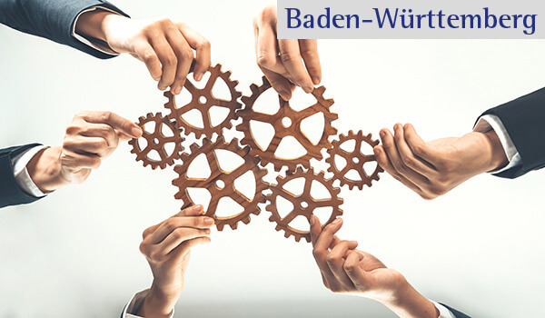 Ein Symbolbild, in dem von allen Seiten Hände jeweils ein Zahnrad halten. Die Zahnräder werden so gehalten, dass sie in der Mitte ineinander greifen.