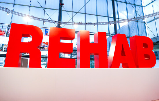 In roten großen Buchstaben steht das Wort "REHAB" auf einem weißen Podest  vor einer verspiegelten Wand.