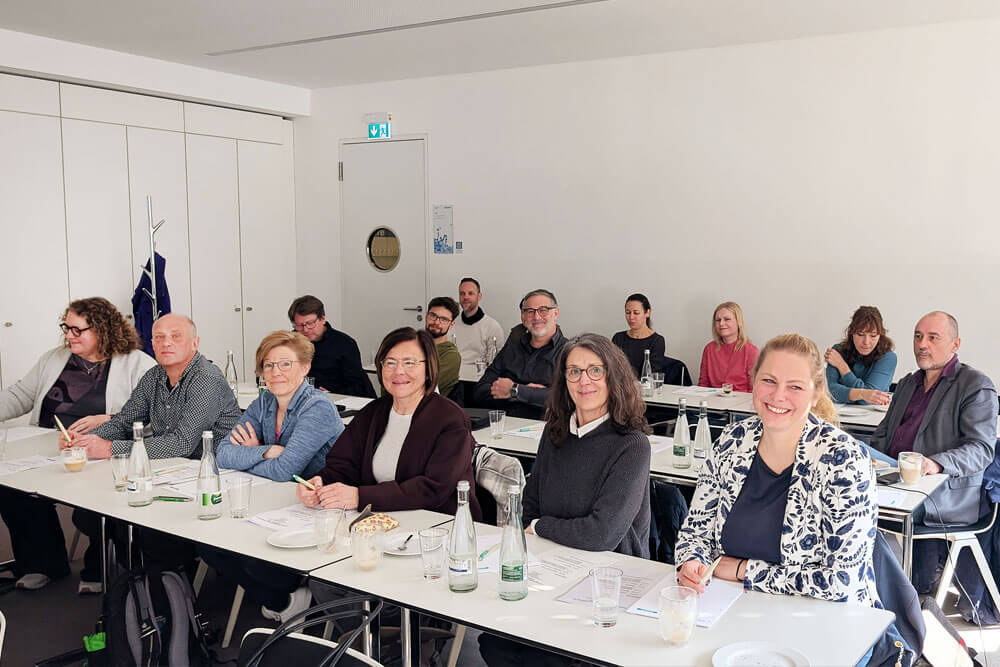 Aufnahme eines Seminarraums, in dem die Teilnehmer an langen Tischreihen sitzen.