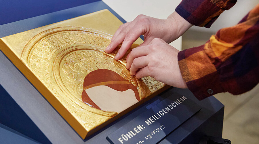 Nahaufnahme einer goldenen Heiligenschein-Plastik, die von zwei Händen ertastet wird.