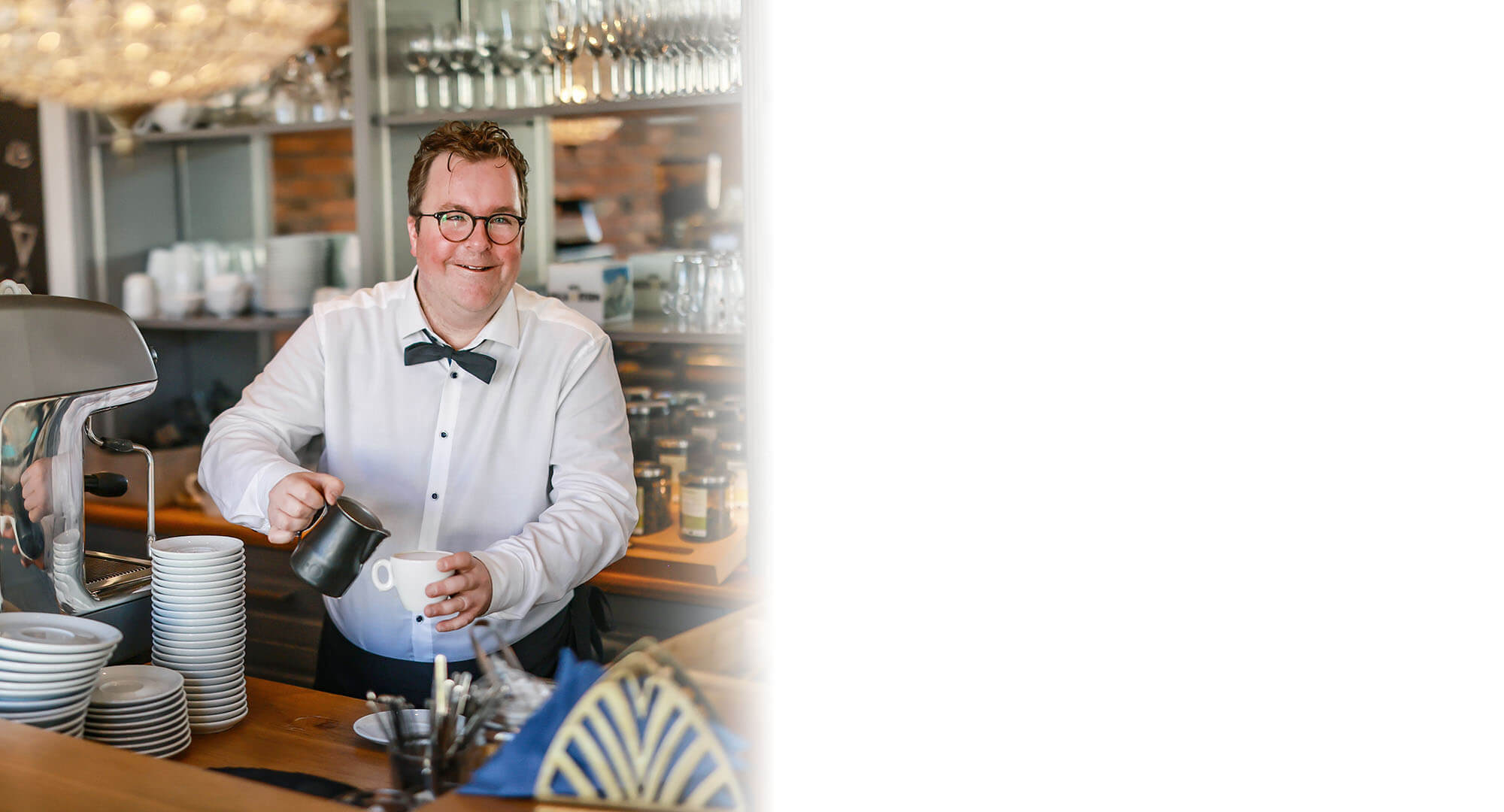 Arne Krüger-Brörken an der Kaffeemaschine l © Rupert Oberhäuser Arne Krüger-Brörken lächelt in die Kamera während er hinter dem Tresen eine Kaffee zubereitet.