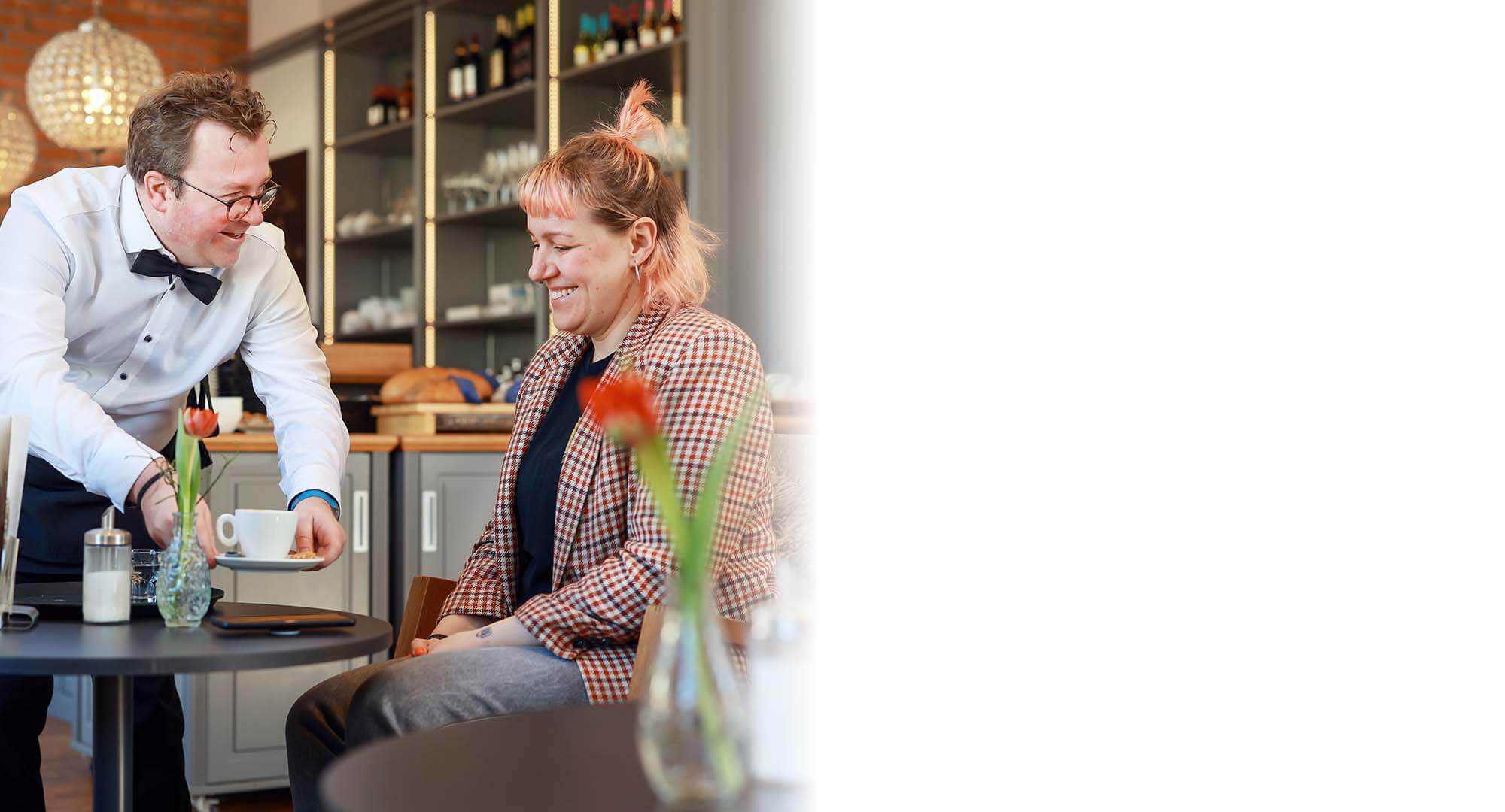Arne Krüger-Brörken mit Gast l © Rupert Oberhäuser Arne Krüger-Brörken stellt eine Kaffeetasse auf einen Cafétisch vor einem Gast ab.