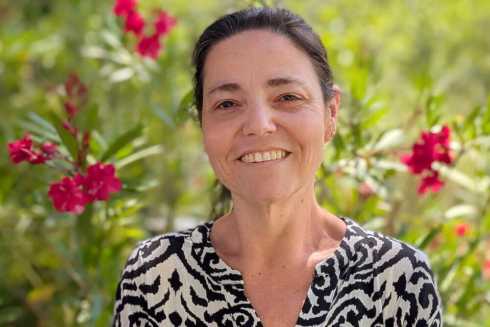 Frau Albiez | © Monika Kleusch Frau Albiez steht vor einer Reihe von Blumen im Hintergrund.