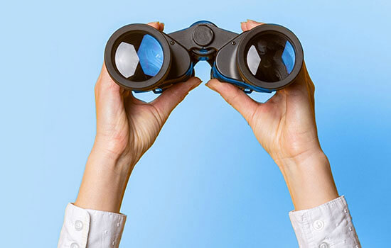 Ein Fernglas das von zwei Händen gehalten wird. 