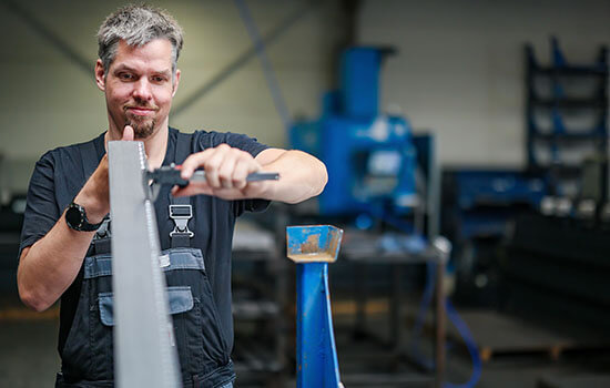 Ein Arbeiter vermisst eine Metallleiste in einer Werkstatt.